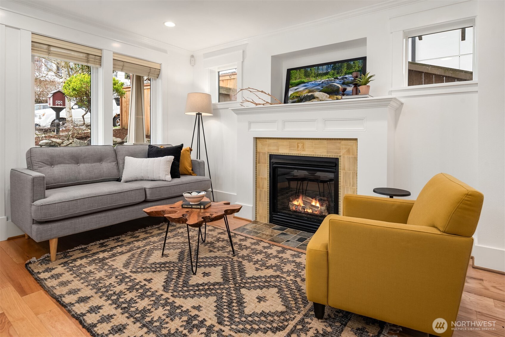 Staged living room with a lit fireplace, gray sofa, mustard armchair, and patterned rug.