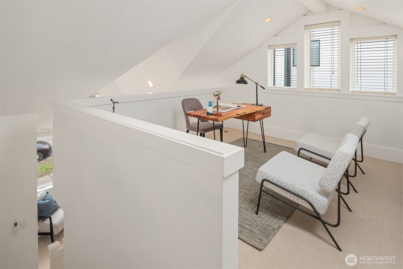 Attic office with a wooden desk, two chairs, and three windows beneath a sloped ceiling.
