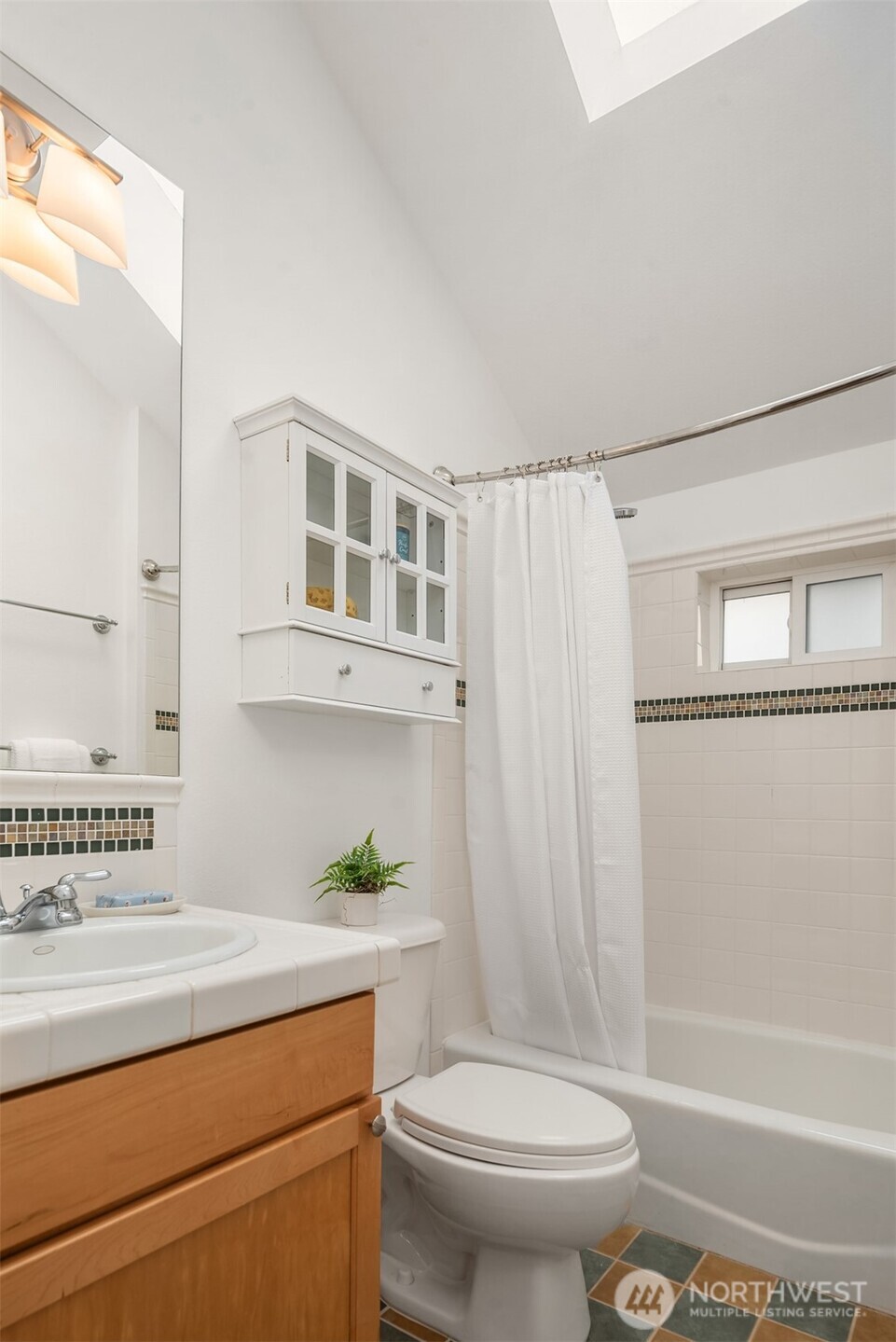 Bathroom with a wood vanity, wall-mounted cabinet, and white-curtained tub beside a high window.