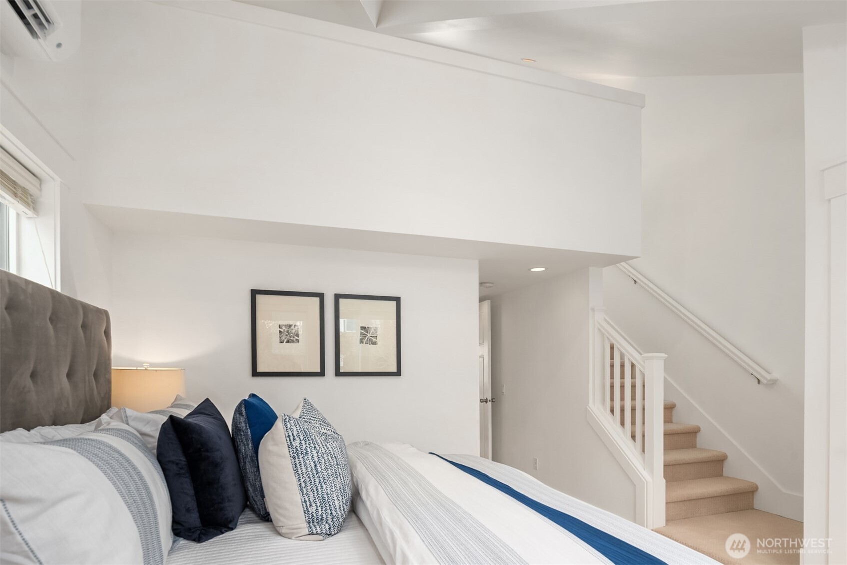Furnished bedroom with blue-and-white bedding and a carpeted staircase beside the bed.