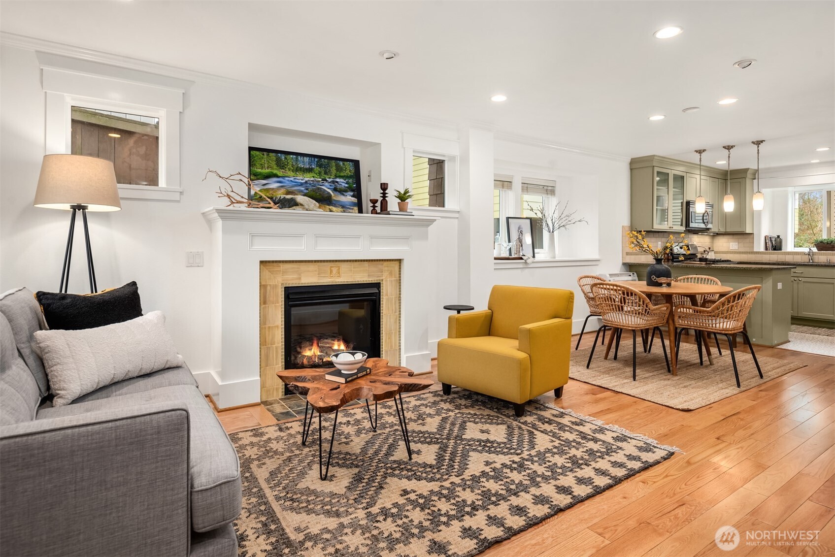 Living room with a tiled fireplace, gray sofa, mustard-yellow chair, and adjoining dining area.