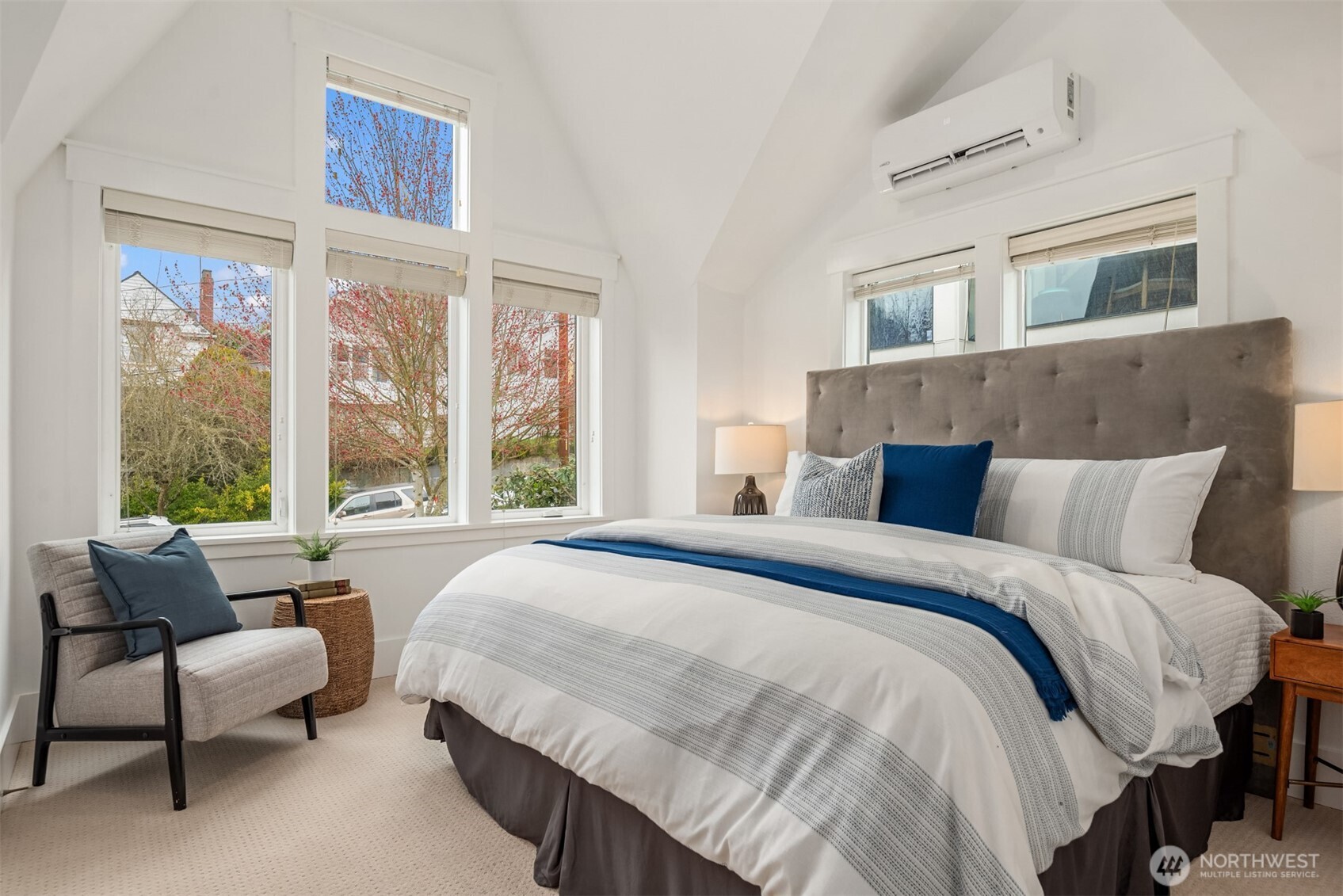 Bedroom with a vaulted ceiling, tall windows, and a large bed dressed in white and blue.