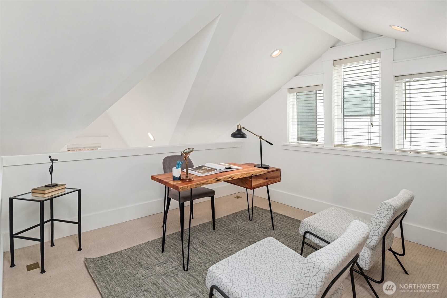 Furnished attic office with a live-edge desk, sloped ceiling, and patterned lounge chairs.