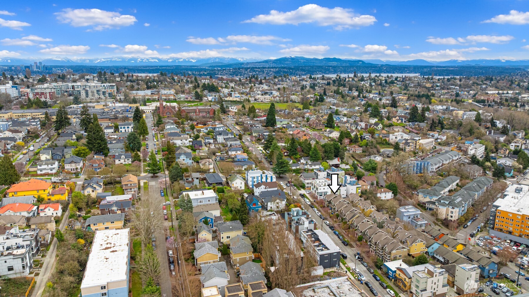 Aerial Seattle neighborhood with the marked home, distant city, and snow-capped mountains.