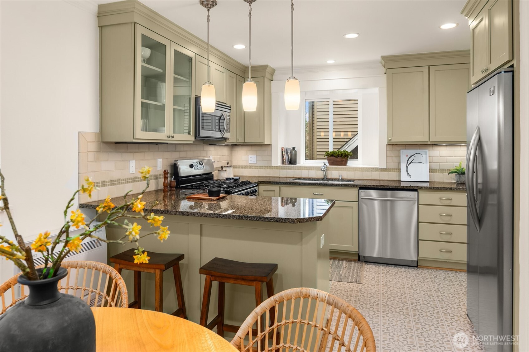 Kitchen with sage-green cabinets, granite counters, stainless steel appliances, and patterned tile flooring.