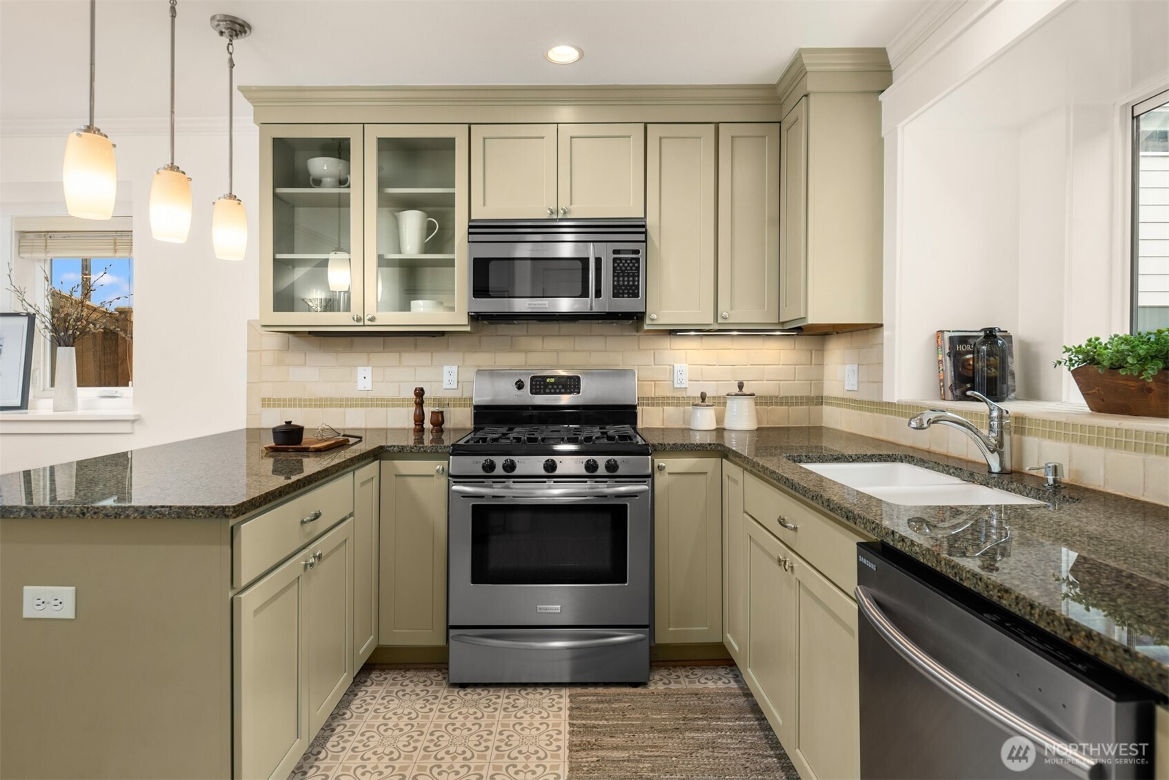Kitchen with sage-green cabinets, granite counters, stainless steel appliances, and patterned tile flooring.