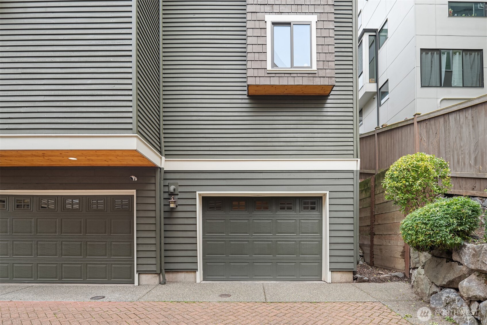 Gray-sided home exterior with two garage doors and a shingled window projection above.