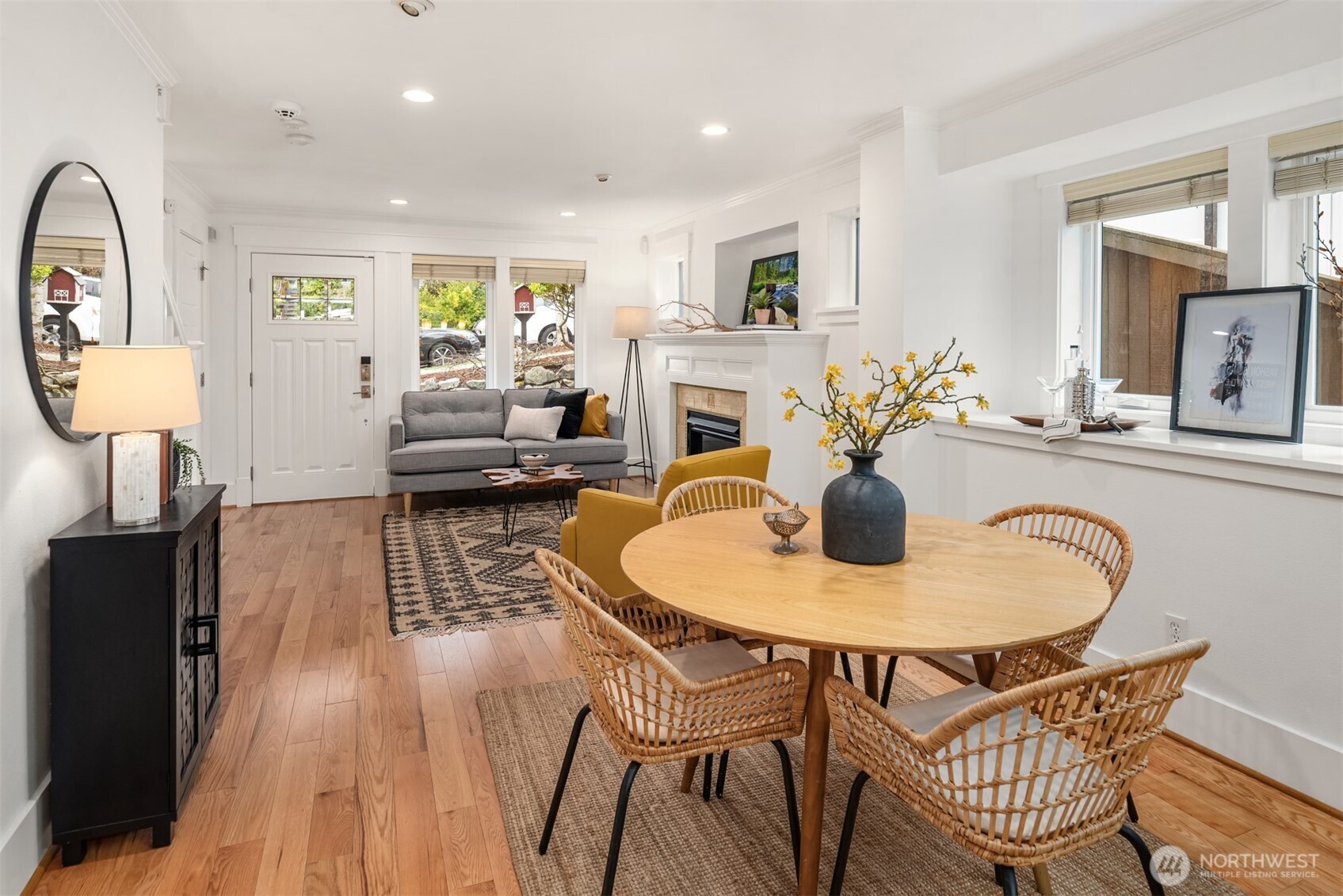 Open-plan dining and living room with a round wood table, woven chairs, gray sofa, and fireplace.
