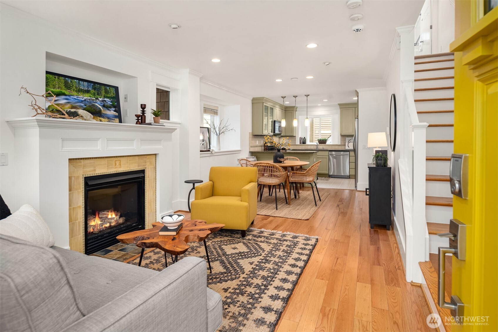 Open-plan living room with a tiled fireplace, mustard-yellow armchair, and view into the dining area and kitchen.
