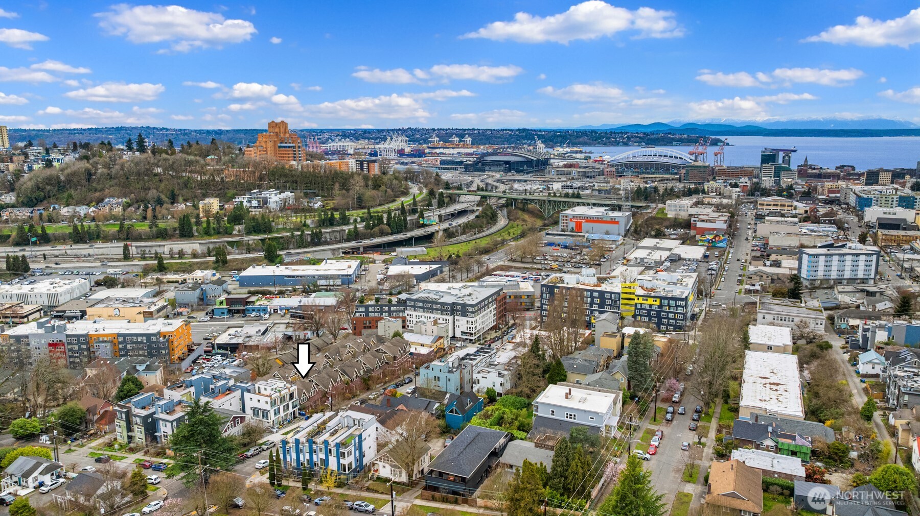 Aerial view of the arrow-marked home amid Seattle neighborhoods, with downtown, waterfront, and mountains beyond.