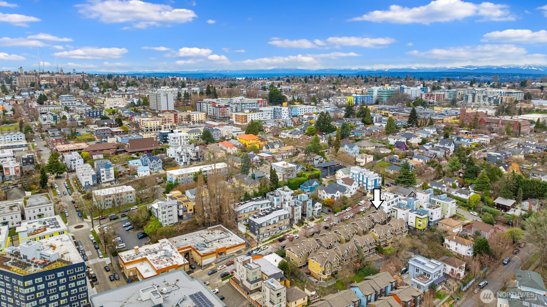 Aerial Seattle neighborhood with an arrow pointing to a row of townhouses and distant mountain views.
