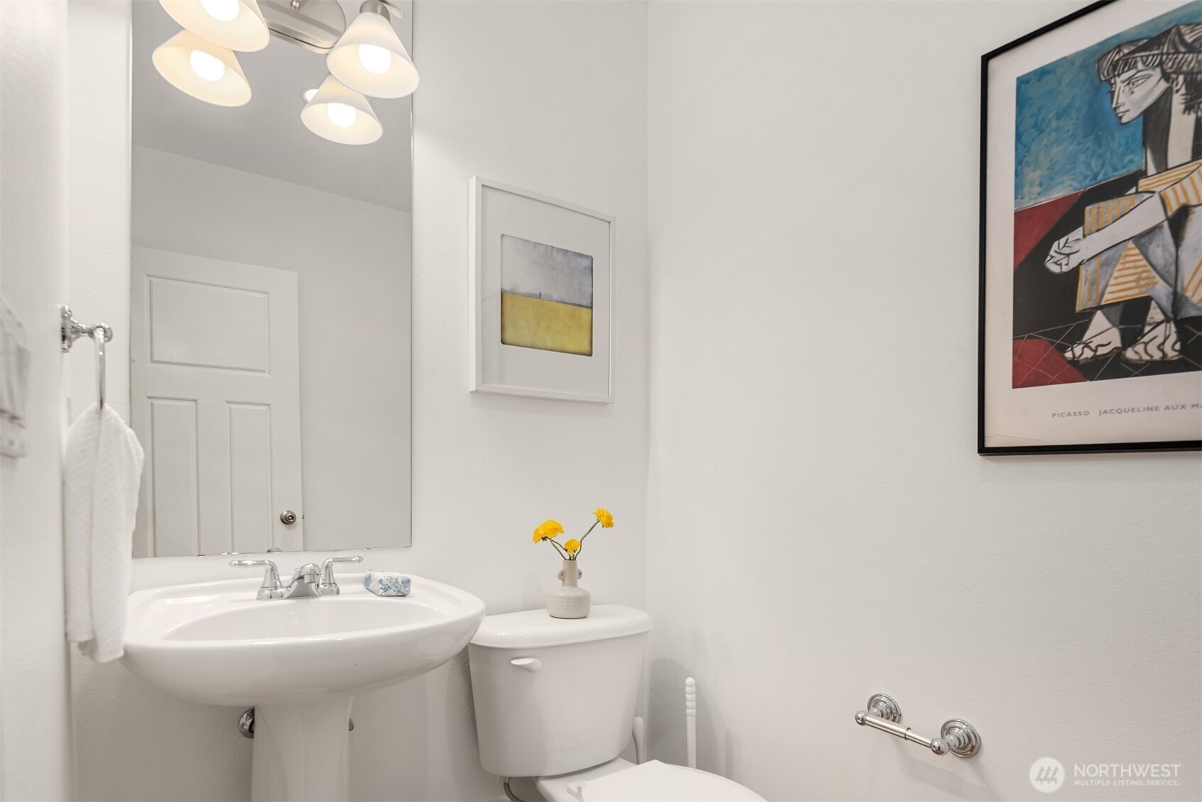 Bright bathroom with a pedestal sink, toilet, and framed colorful artwork.