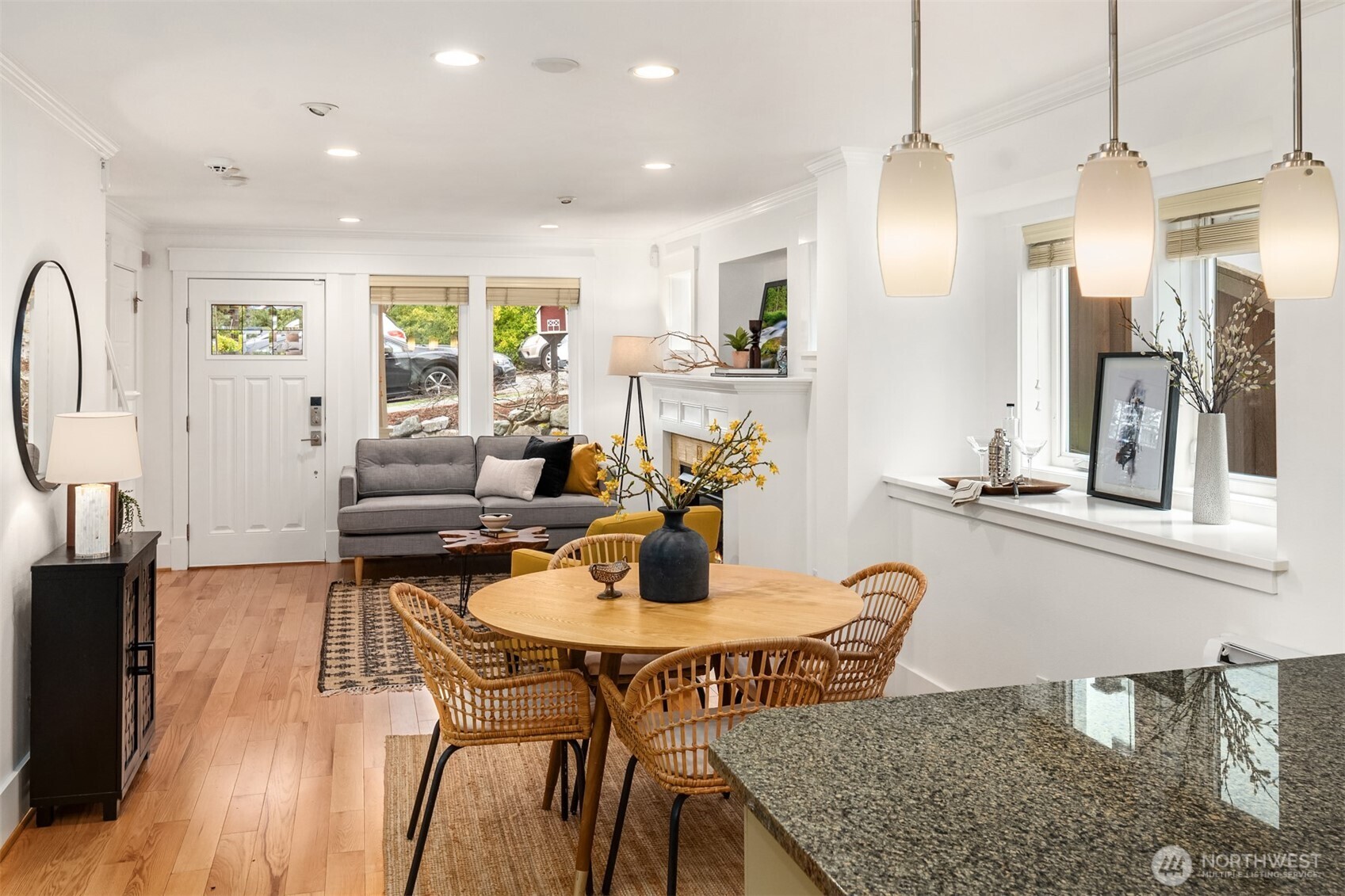 Dining and living area with a round wood table, woven chairs, gray sofa, and white fireplace.