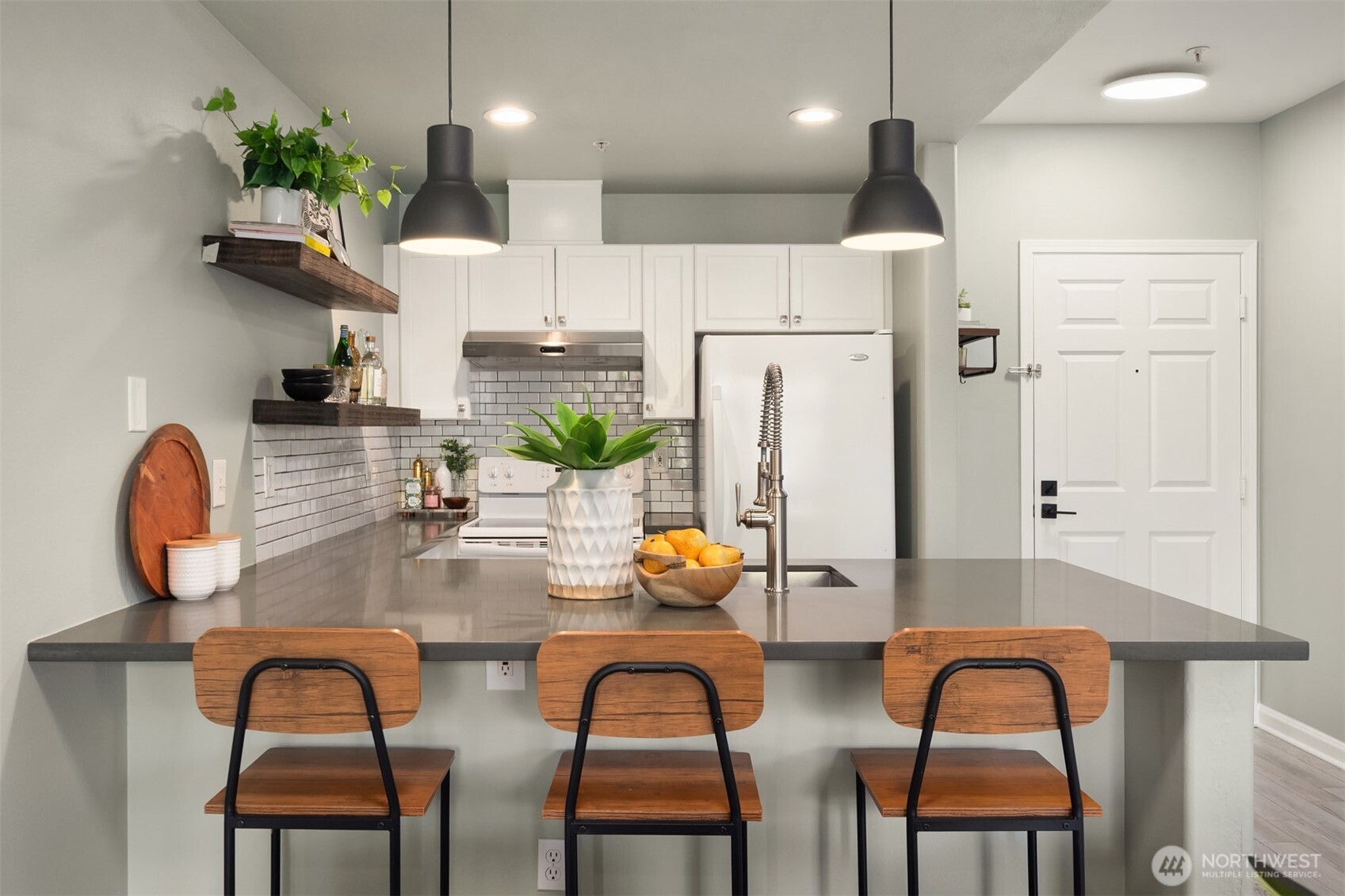 Kitchen with a gray island, three wooden stools, white cabinets, and a subway-tile backsplash.