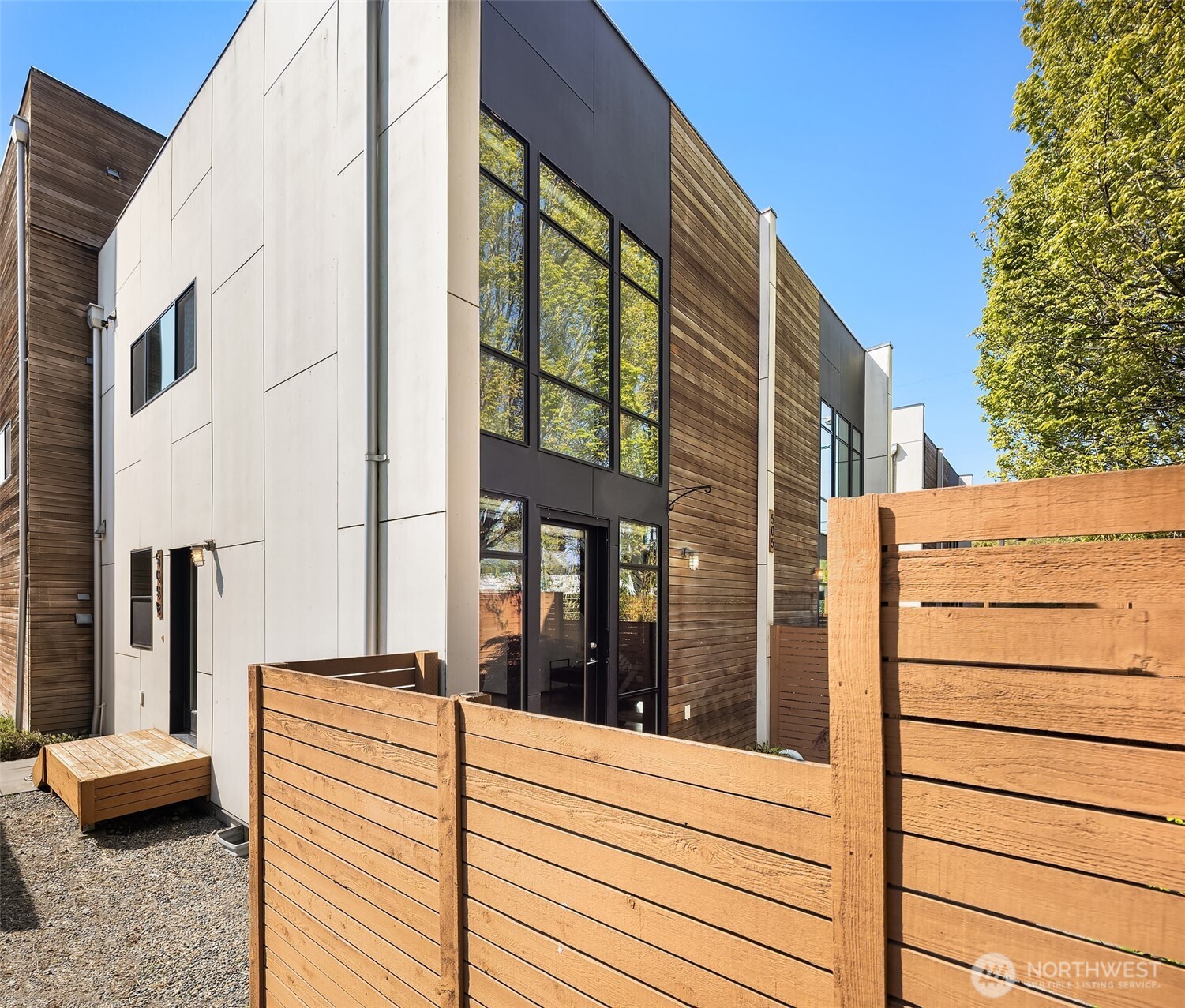 Modern home with charcoal and wood siding behind a tall wooden privacy fence.