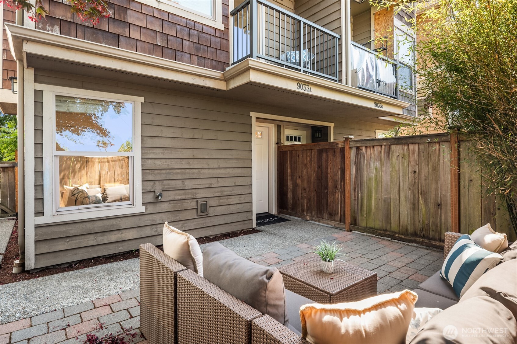 Fenced patio with wicker seating and paved courtyard beside the home's entrance.
