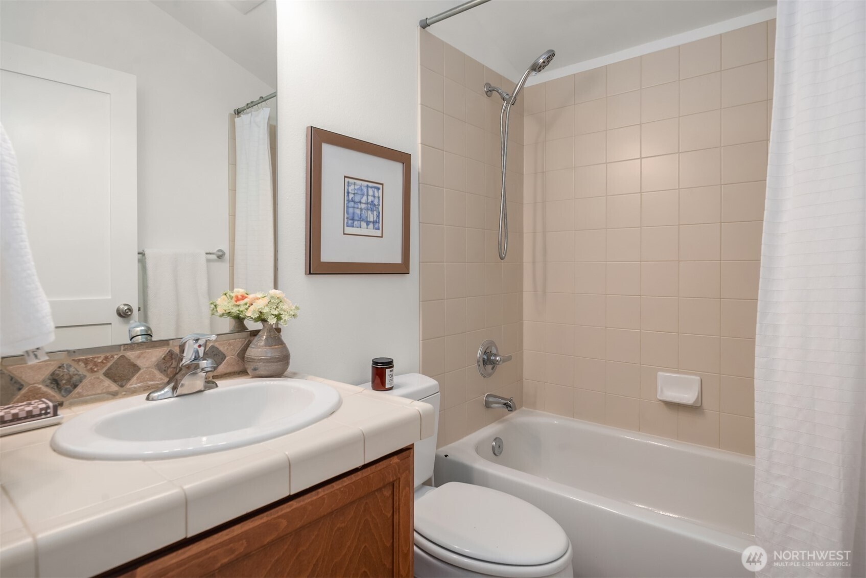 Bathroom with a wood vanity and white sink beside a beige-tiled bathtub and shower.