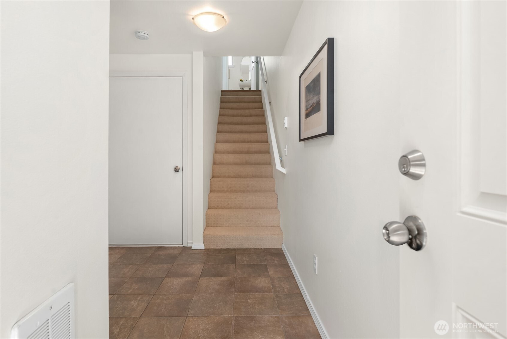 Entry hall with brown tile flooring and carpeted stairs leading to an upper level.