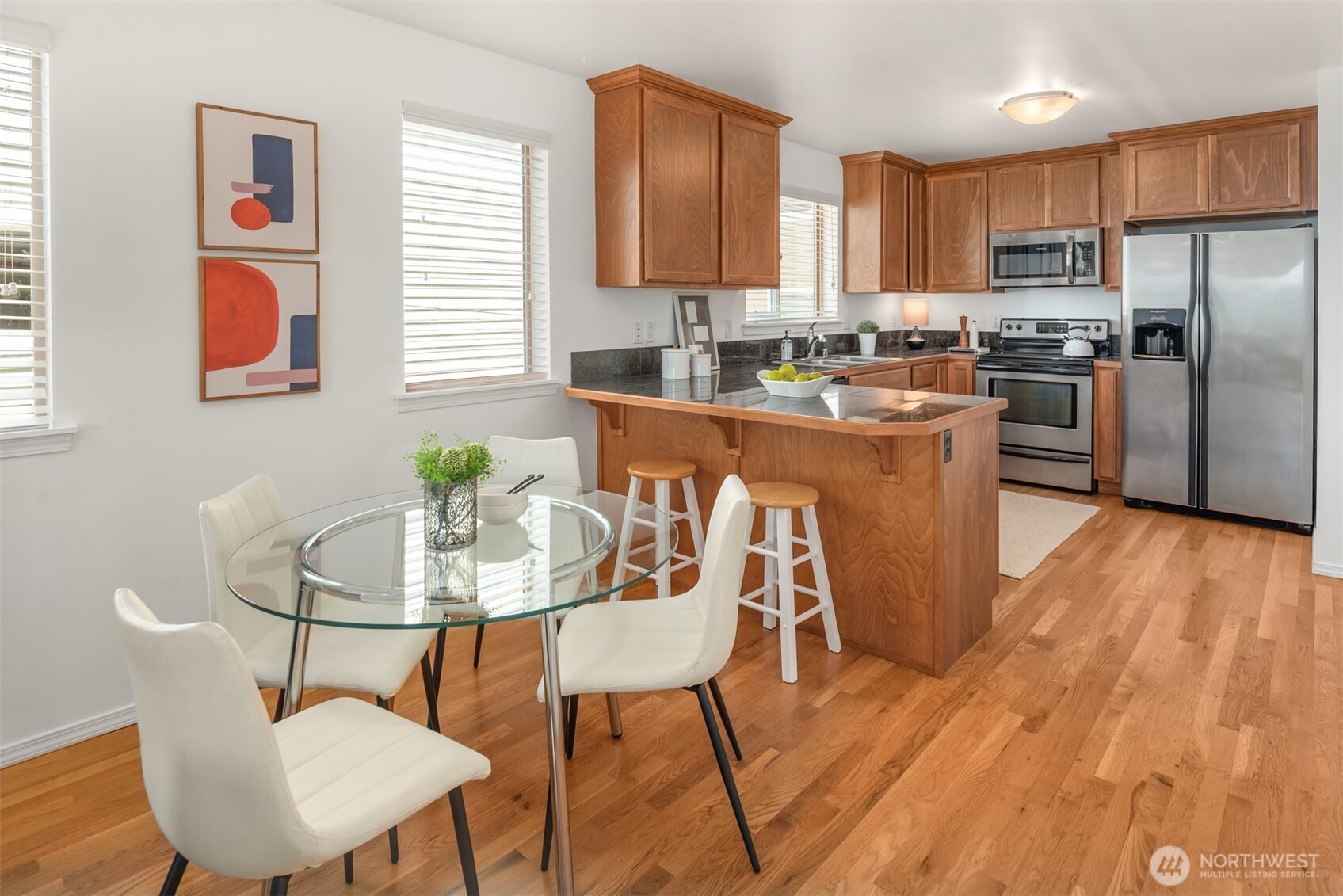 Kitchen and dining area with warm wood cabinetry, a large island, stainless steel appliances, and a glass table.