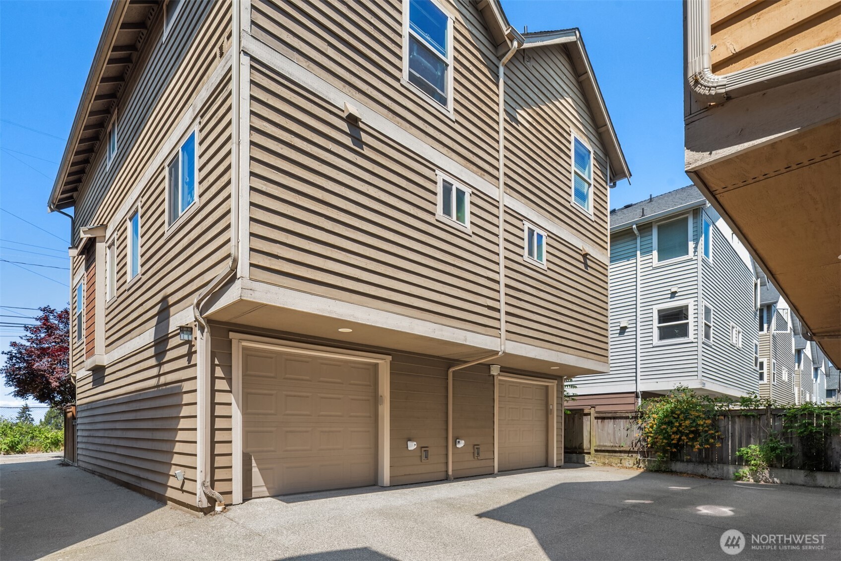 Tan-sided townhome with two garage doors opening onto a paved driveway.