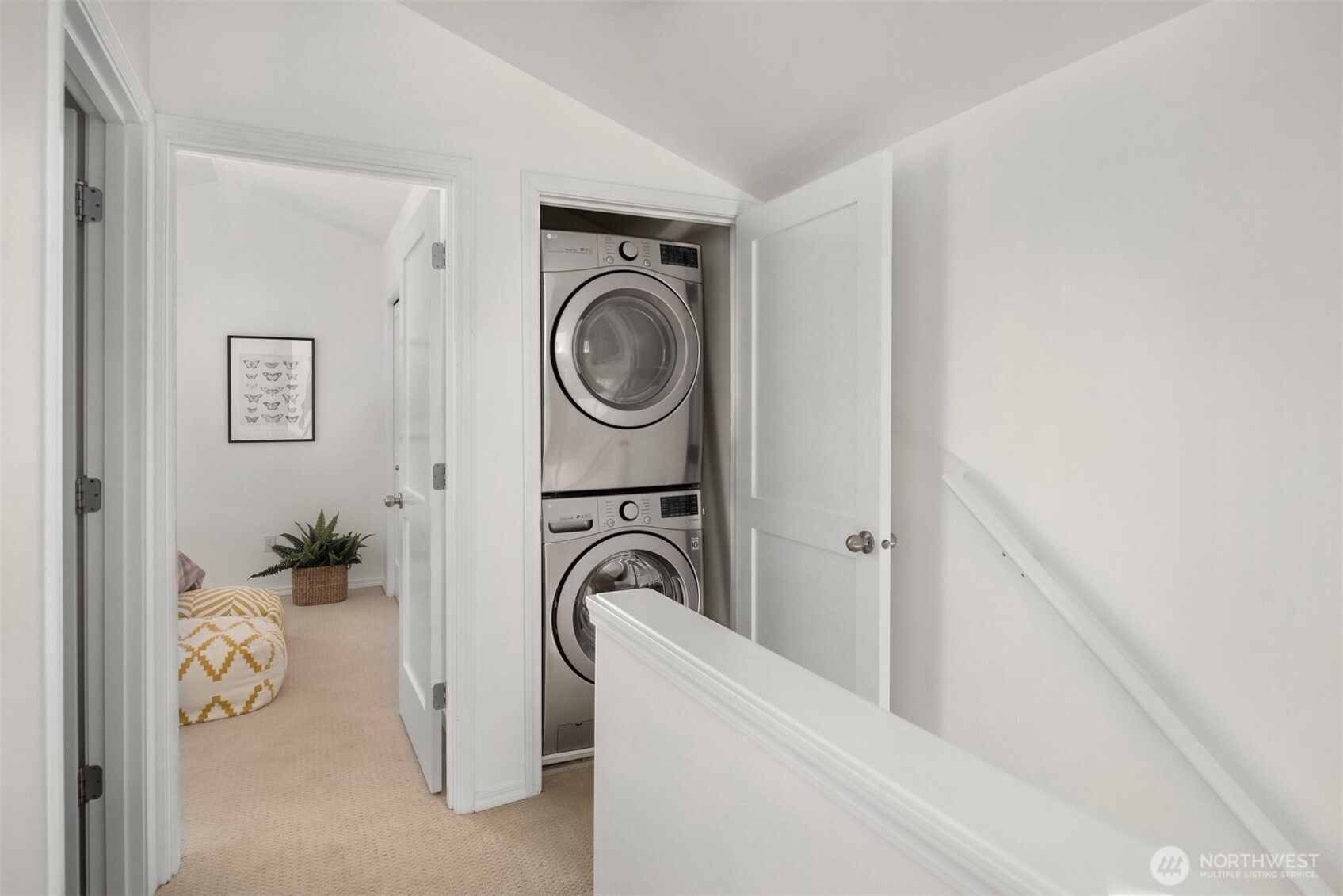 Stacked washer and dryer in a hallway closet beside a carpeted landing.