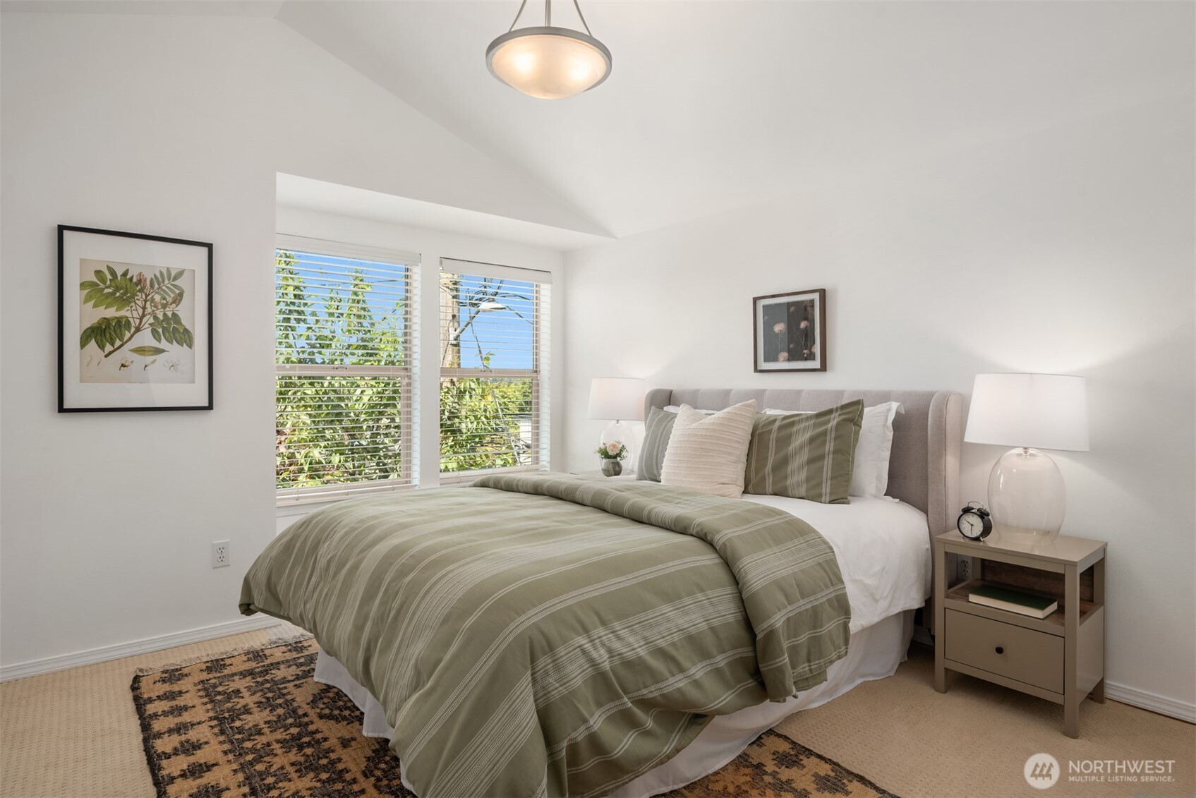 Bedroom with a large sage-green striped bed beside two windows with blinds.