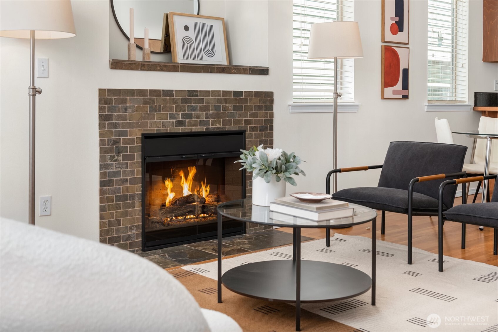 Living room with a lit tile-surround fireplace, glass coffee table, and black lounge chairs.