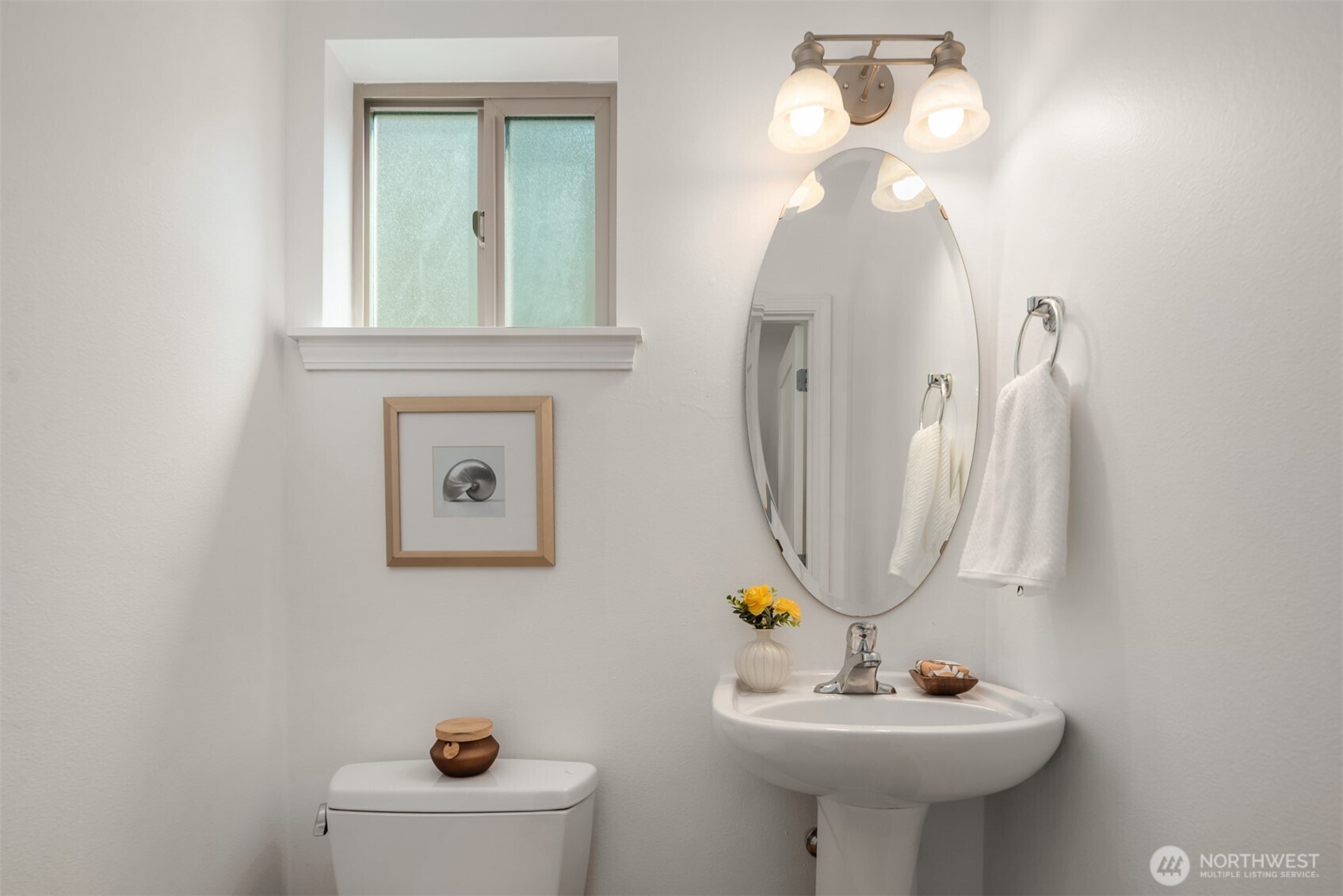 Bathroom with a white pedestal sink, oval mirror, and frosted window.