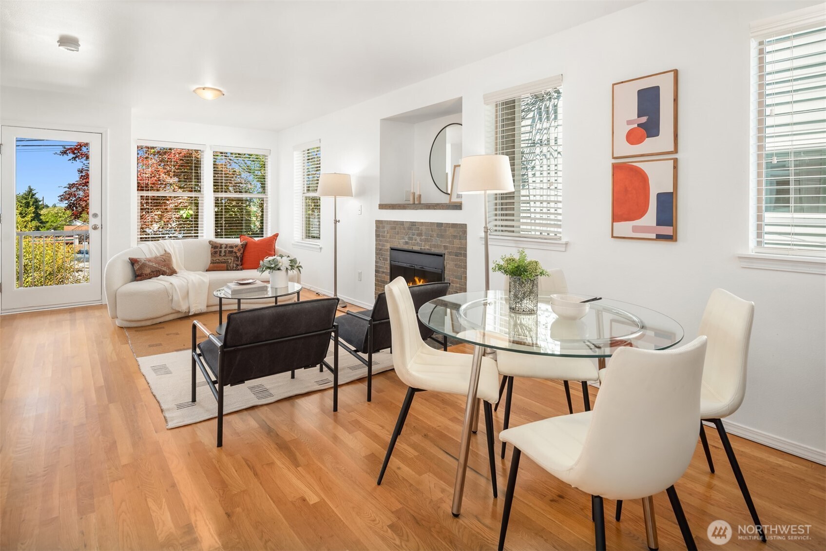 Open living and dining room with hardwood floors, a tiled fireplace, and a glass dining table.