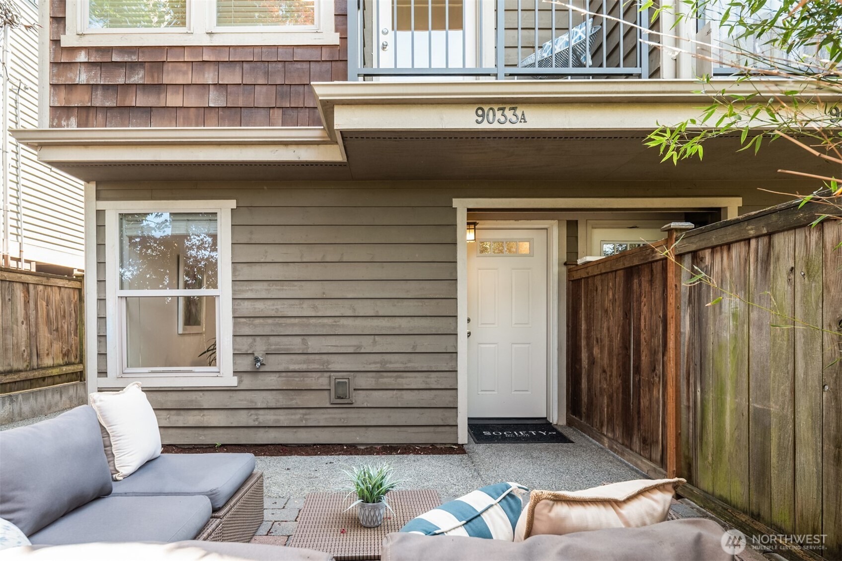 Home entrance opening onto a fenced patio with outdoor seating and the address number 9033A above the door.