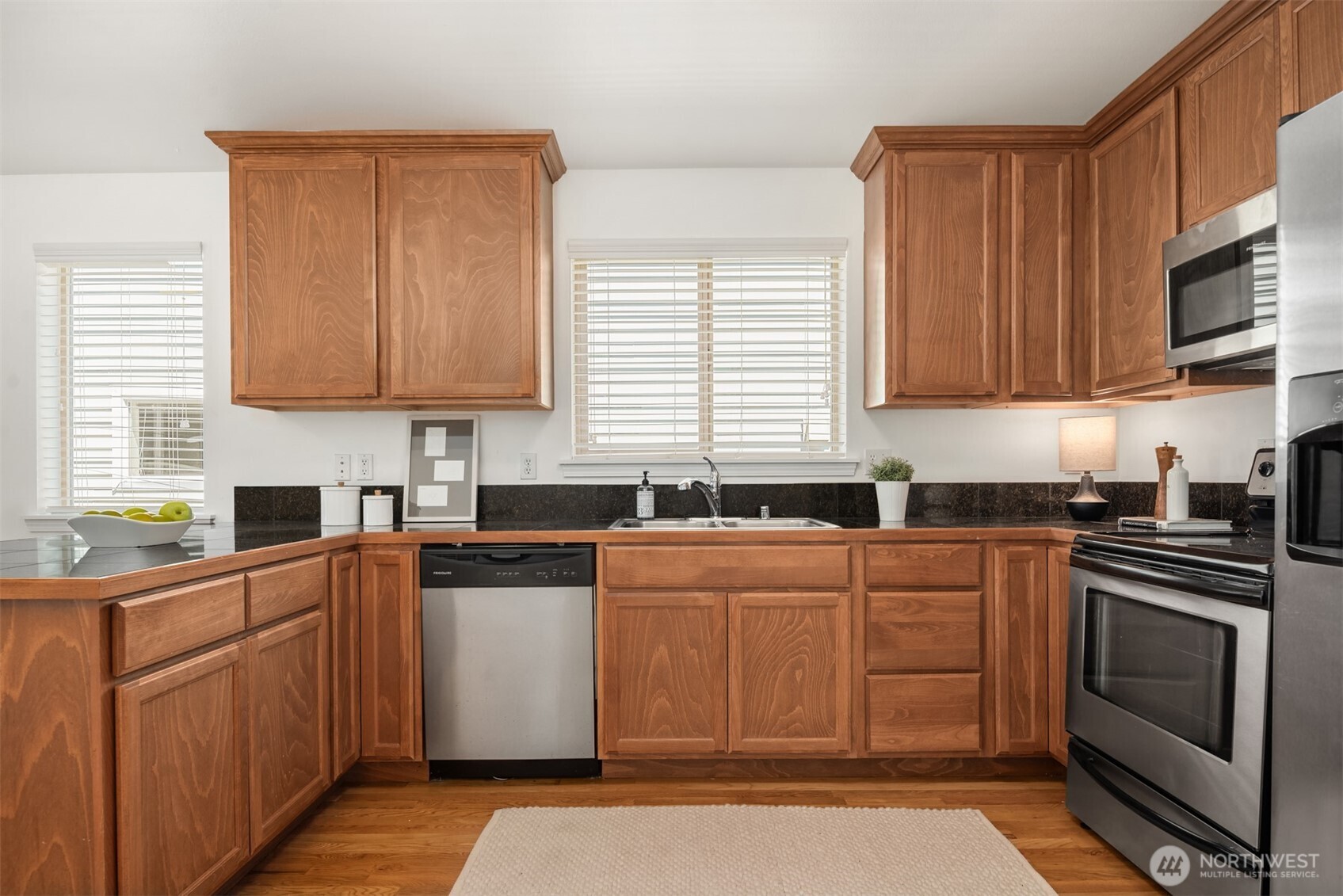 Kitchen with warm wood cabinets, dark countertops, stainless steel appliances, and a sink beneath the window.