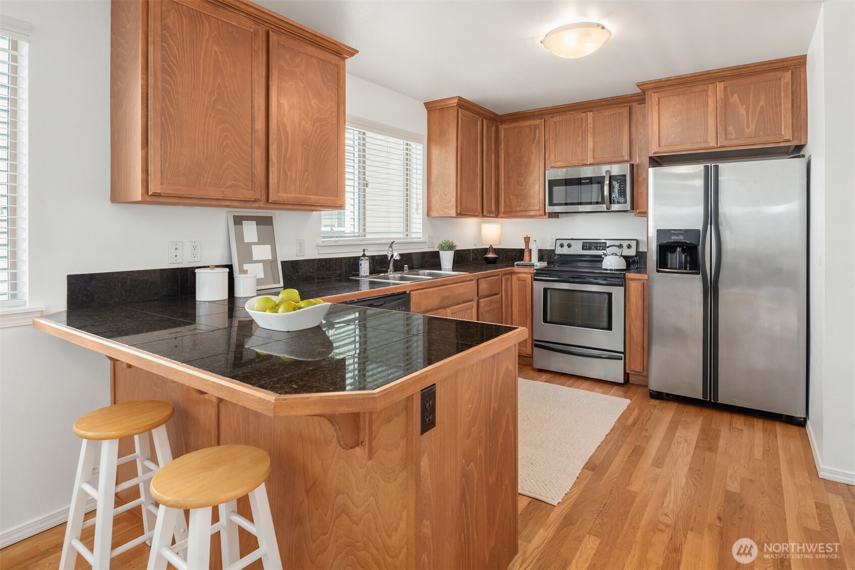 Kitchen with wood cabinets, dark stone counters, a peninsula with stools, and stainless steel appliances.