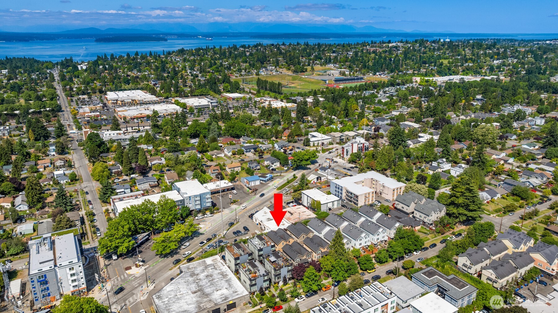 Aerial view of the home marked by a red arrow, with Seattle neighborhoods, water, and distant mountains.