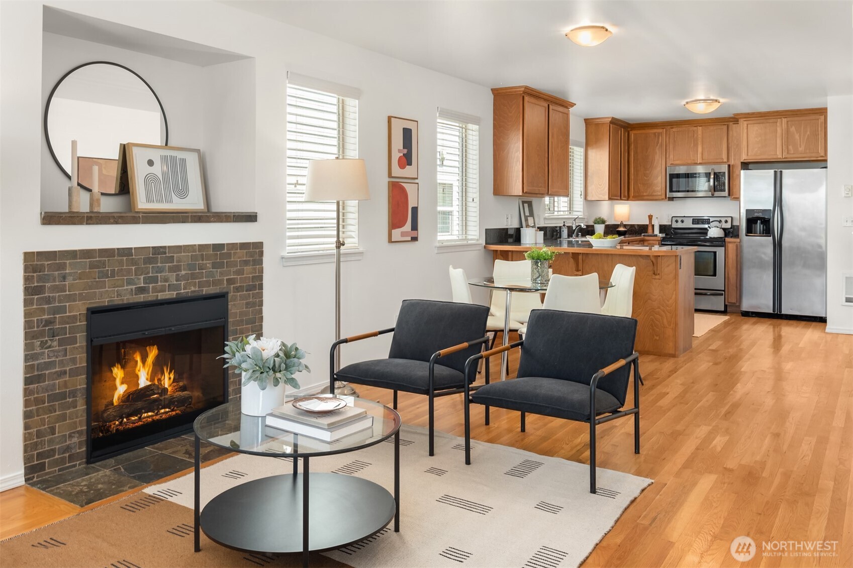 Living room with a stone-tile fireplace, dark armchairs, hardwood floors, and an open kitchen.