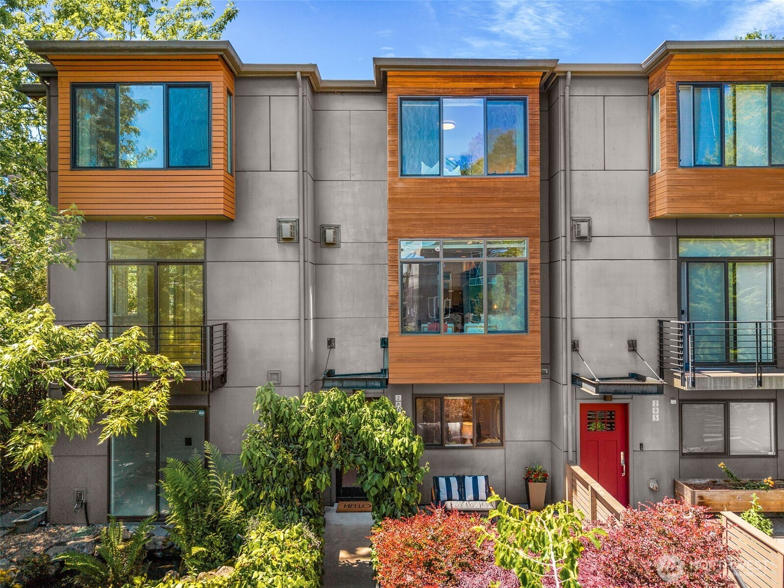 Modern townhouse with wood-clad window bays, a red front door, and landscaped garden.