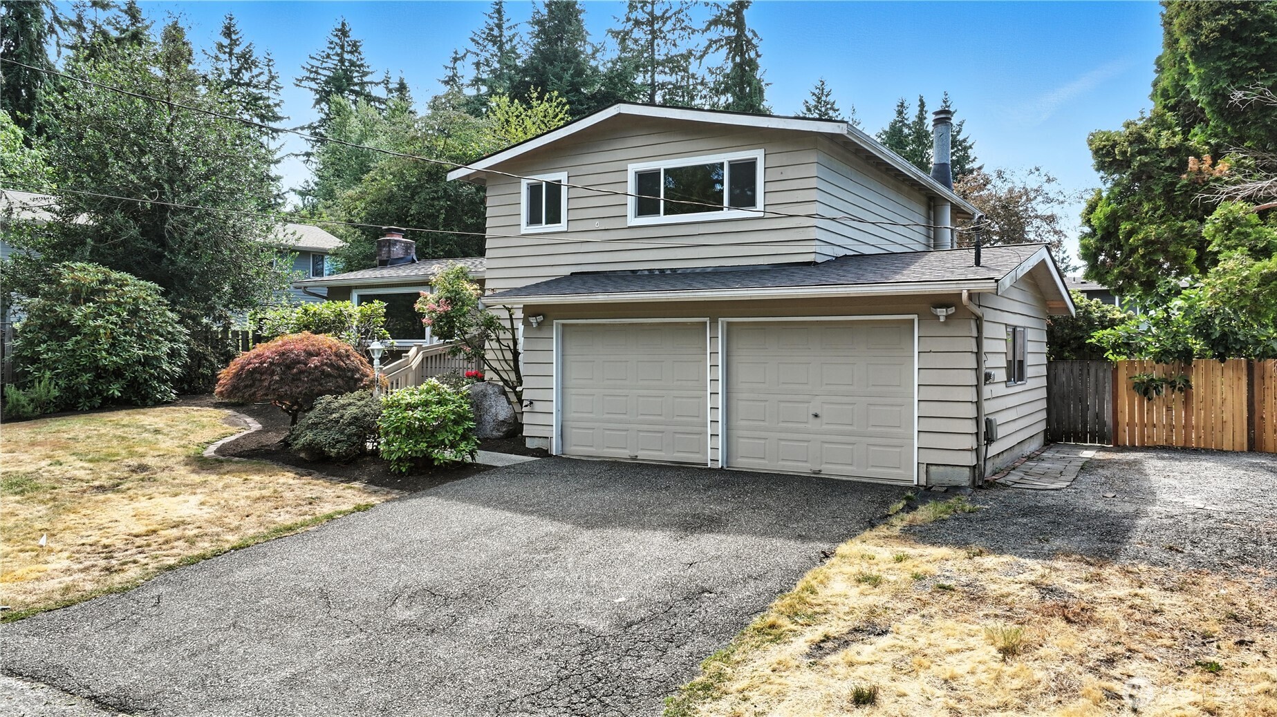 Two-story beige house with a double garage, wide driveway, and landscaped front yard.