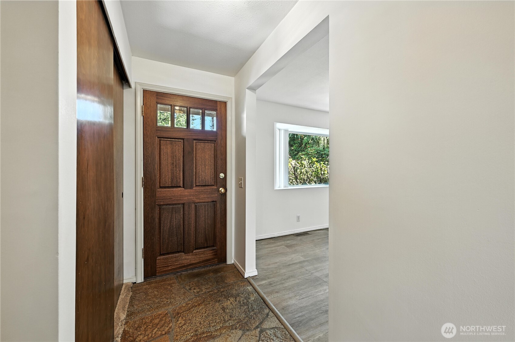 Entryway with a dark wood front door, stone tile floor, and adjacent empty room.