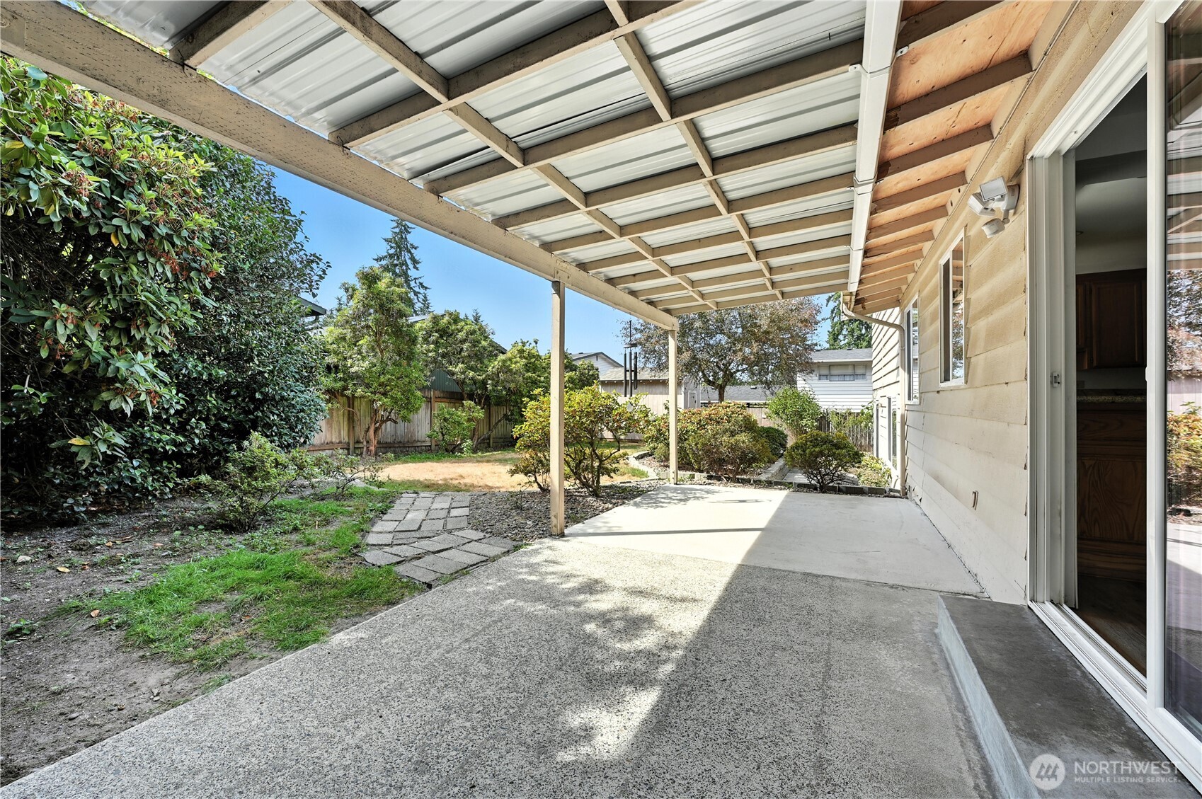 Covered concrete patio beside a landscaped, fenced backyard with a stepping-stone path.