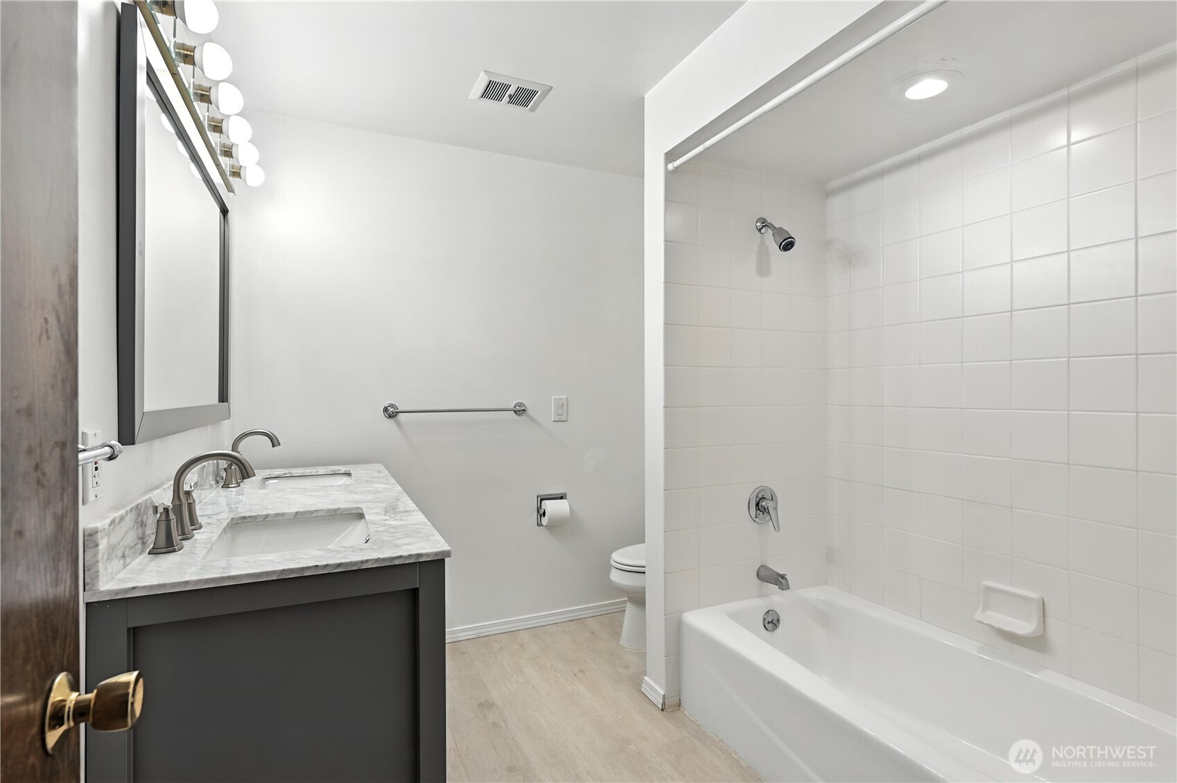 Bathroom with a marble double-sink vanity beside a white tiled tub and shower.