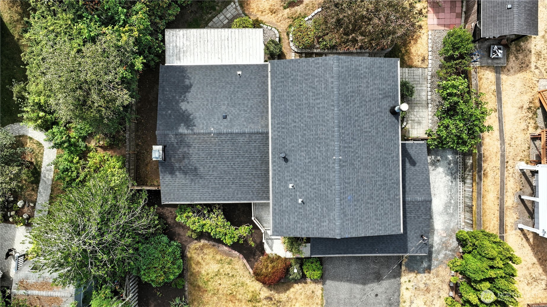 Aerial view of a home with a broad dark roof and landscaped garden paths.