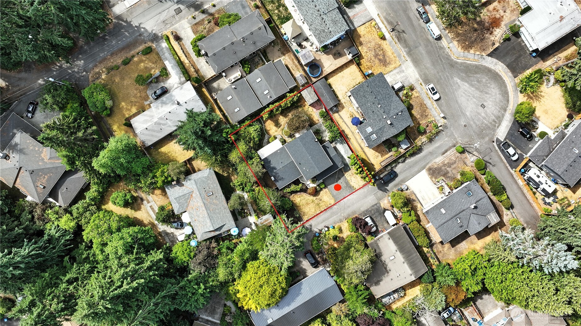 Aerial view of a home and its red-outlined lot, with mature trees and neighboring houses.