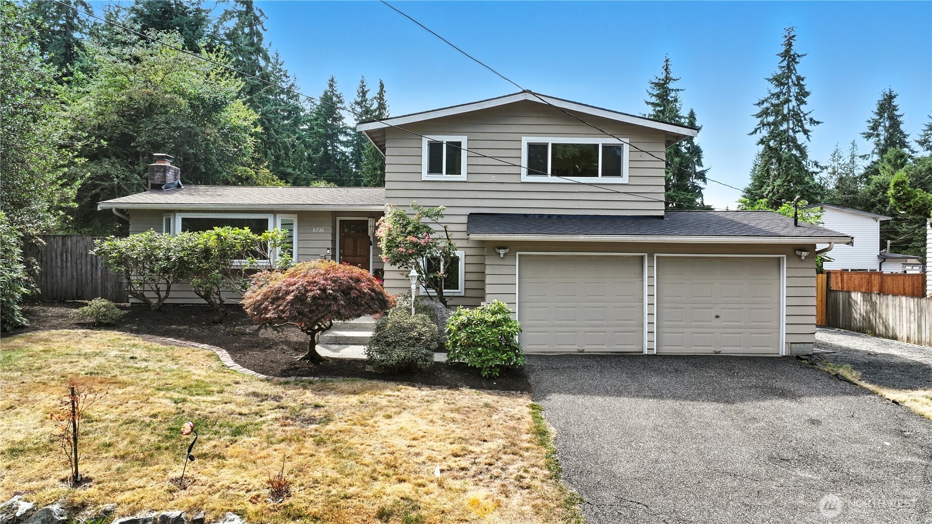 Split-level home with a two-car garage, landscaped front yard, and wooded surroundings.