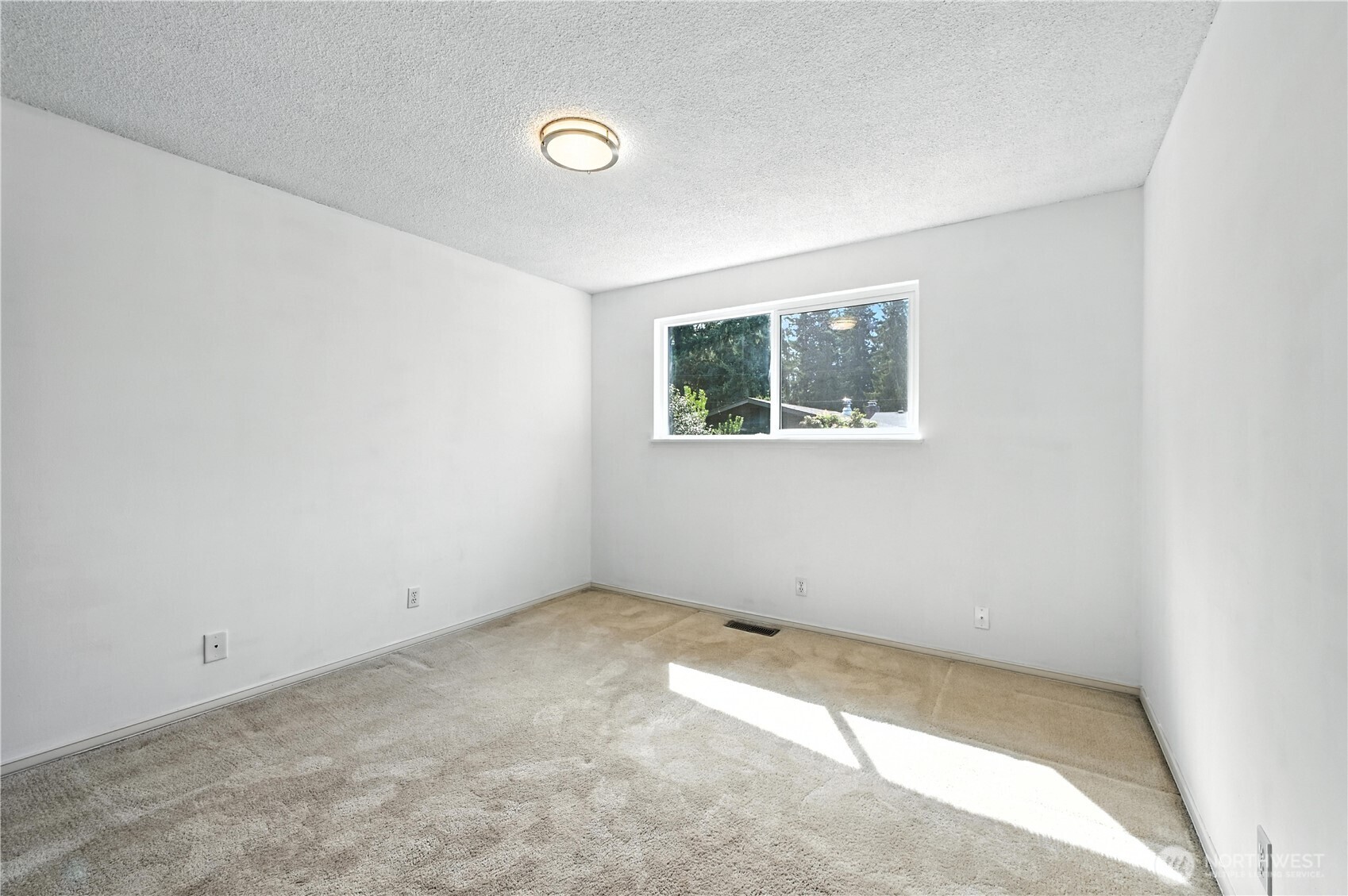 Empty carpeted room with white walls, a small window, and sunlight across the floor.
