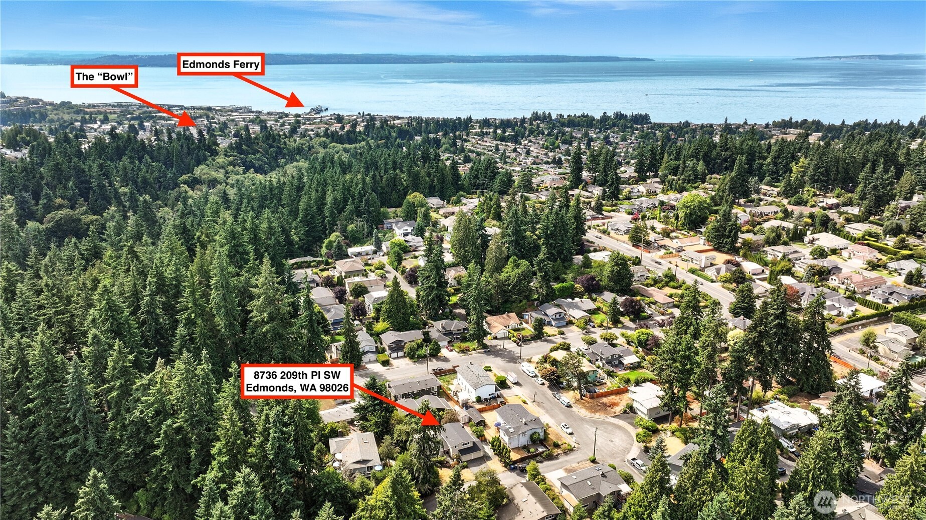Aerial view of 8736 209th Place SW amid wooded neighborhoods, with the Edmonds Ferry and water in the distance.