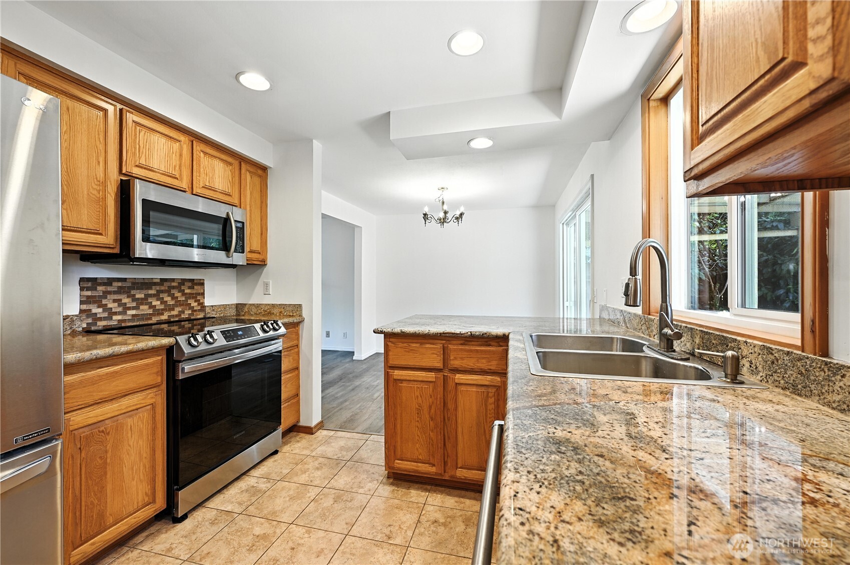 Kitchen with honey-toned wood cabinets, granite counters, a peninsula, and stainless steel appliances.