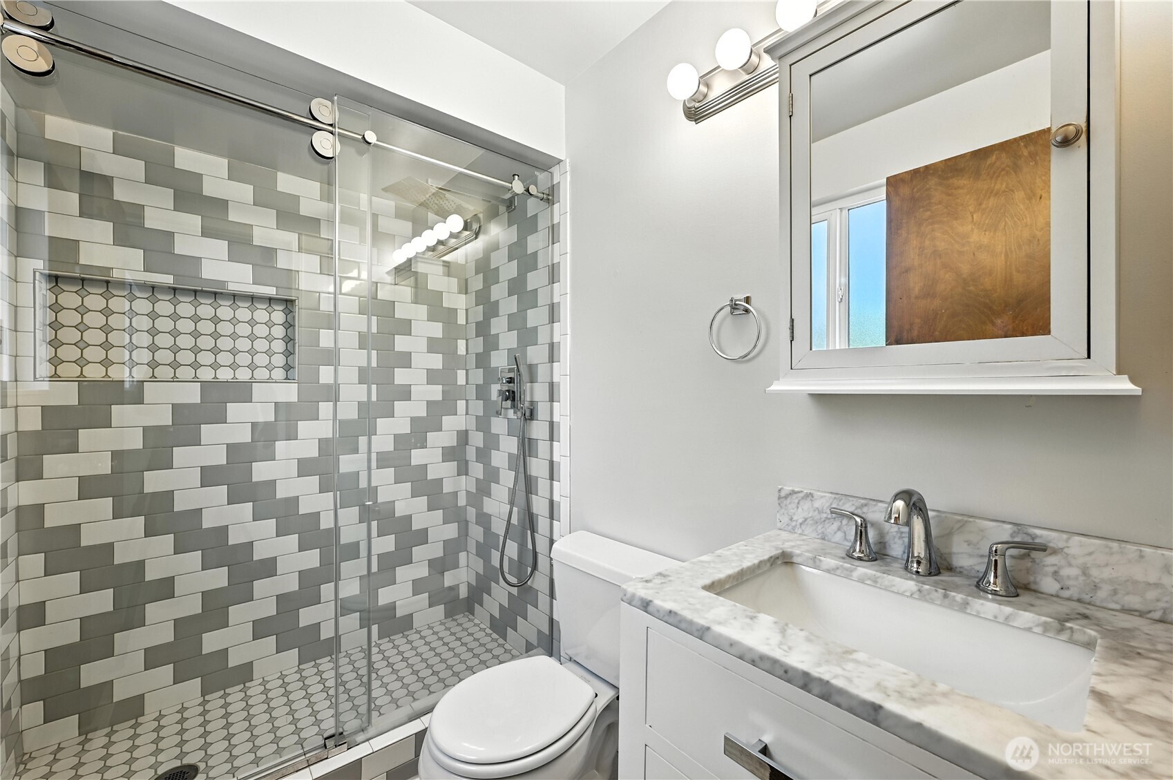 Bathroom with a glass-enclosed tiled shower, hexagonal-tile niche, and marble-topped vanity.