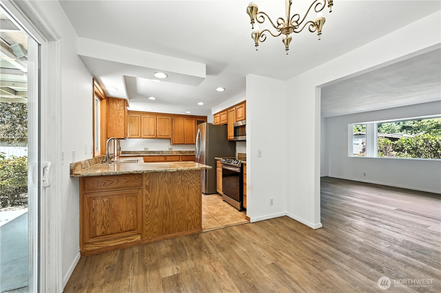 Vacant kitchen with wood cabinets, granite peninsula, and stainless steel appliances opening to an empty room.