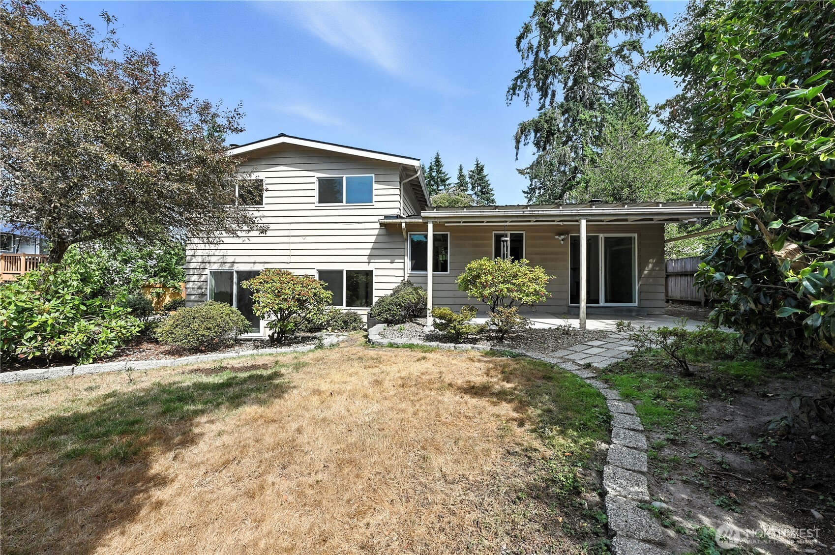 Rear of a split-level house with a covered patio and curved stone path through the backyard.