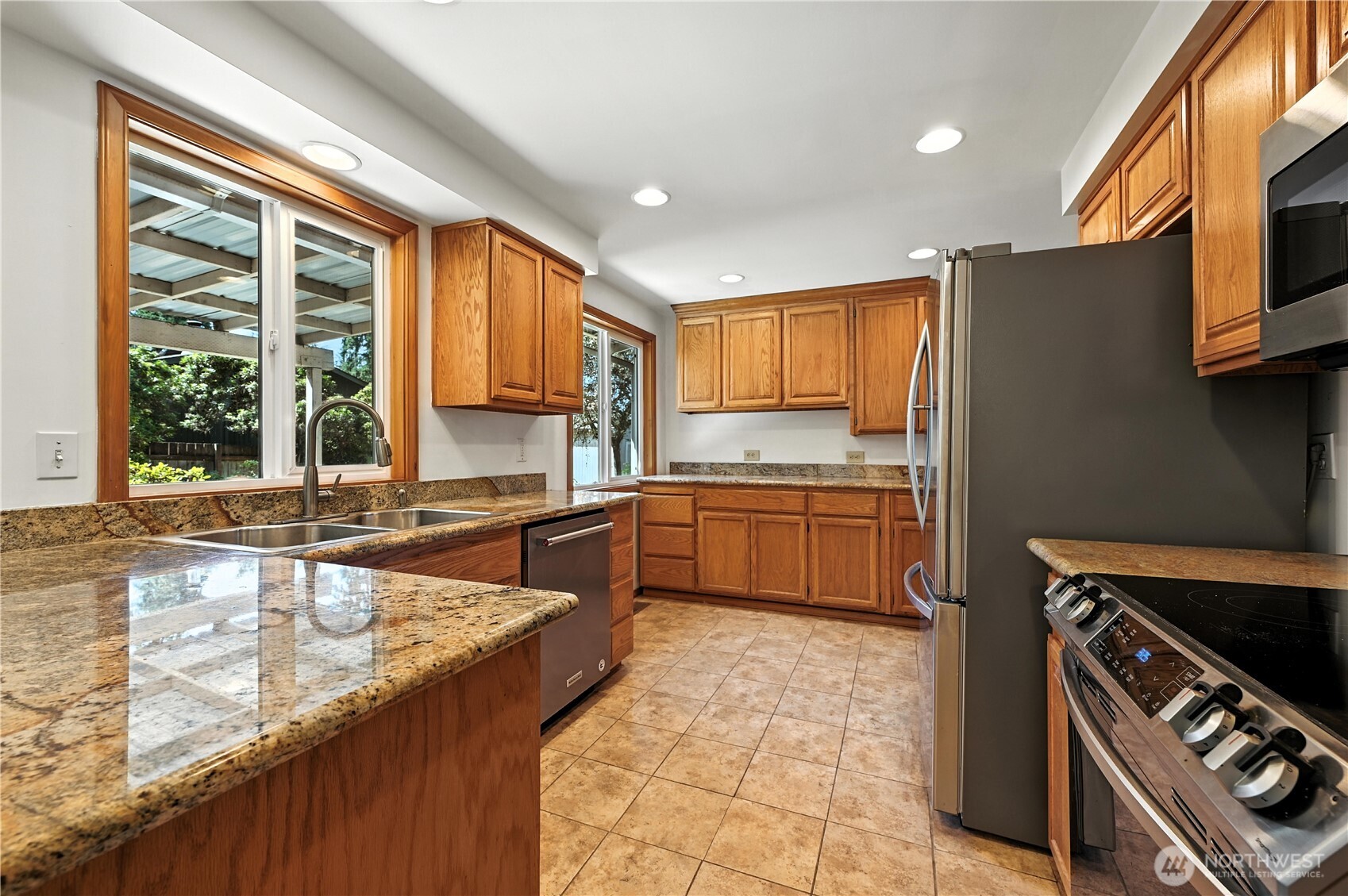 Kitchen with wood cabinetry, granite counters, stainless steel appliances, and windows overlooking a covered patio.