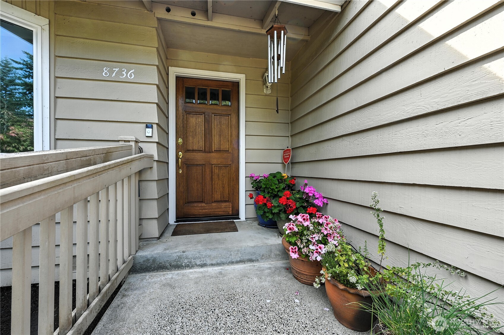 Covered home entry with a dark wood door, concrete steps, and colorful potted flowers.
